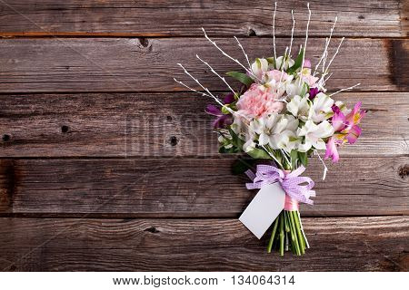 Pink bouquet from gillyflowers and white alstroemeria on old rustic wooden background with a note
