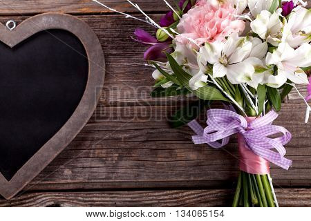 Rustic bouquet from gillyflowers and white alstroemeria on old rustic wooden background with wooden heart