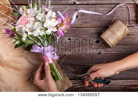 Preparing a rustic bouquet from gillyflowers and white alstroemeria on old rustic wooden background with wooden heart and scissors with paper