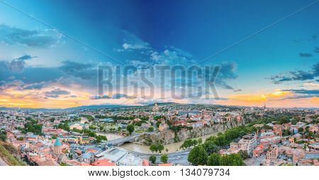 Evening View Of Tbilisi At Colorful Sunset, Georgia. Summer Cityscape. On Panoramic Photograph Visible The Bridge Of Peace, A New Concert Hall, Avlabar Residence - Presidential Administration Of Georgia, Holy Trinity Cathedral Of Tbilisi, Metekhi Church A