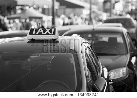 symbol or sign with an inscription of a taxi is located on a car roof on an indistinct background city street of monochrome color