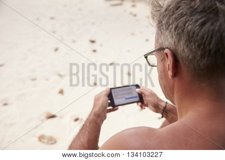 Man using a smartphone on a beach, over shoulder view