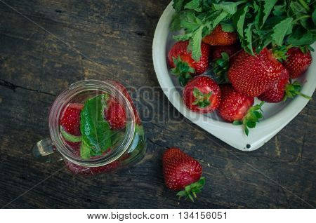 Refreshing summer drink with strawberry in mason jar on the vintage wooden table. Fresh strawberry drink on rustic background. Homemade drink with strawberry and mint in a mason jar. Top view.