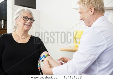 Smiling Patient Looking At Male Doctor Collecting Blood In Syrin