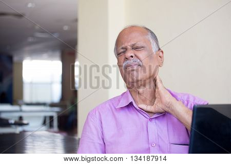 Closeup portrait elderly gentleman in pink shirt with cramping neck pain after using black laptop all day trying to soothe with hand isolated indoors background