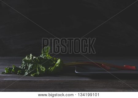 Organic pieplant lying on gray plate and old wooden table with blackboard in background