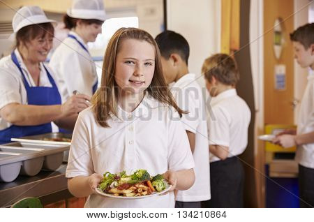 Girl holds a plate of food in school cafeteria, head turned