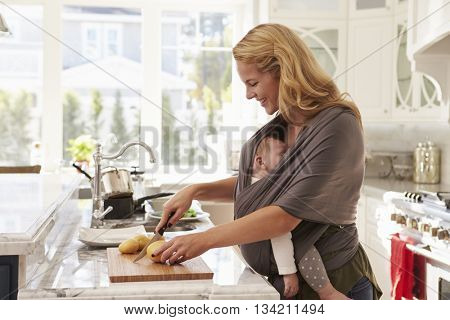 Busy Mother With Baby In Sling Multitasking At Home