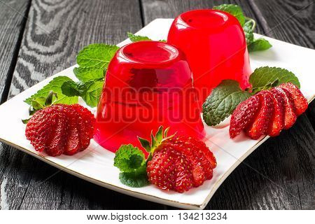 Tasty strawberry jelly and ripe strawberries on plate on a dark wooden table. Selective focus