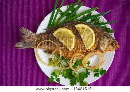 Roasted carp fish with greens on a white plate. The top view