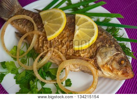 Roasted carp fish with greens on a white plate.