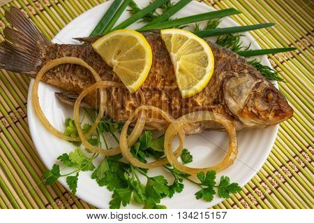 Roasted carp fish with greens on a white plate.