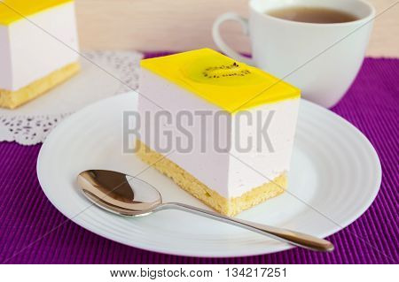 Delicate curd dessert souffle cake with jelly kiwi on a white plate on napkin and cup of tea.