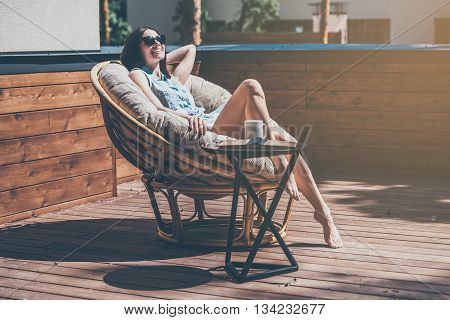 Lazy time in comfortable chair. Beautiful young woman relaxing in a big comfortable chair on her outdoor house terrace