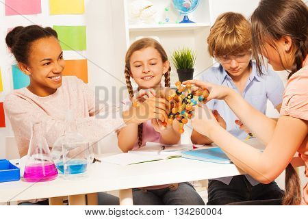 Team of four multi ethnic students assembling molecule model for science project at the chemical laboratory