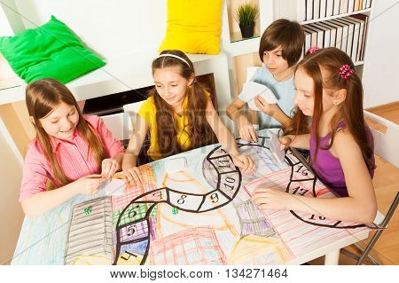 Top view of four kids sitting at the table, playing the tabletop game with cards