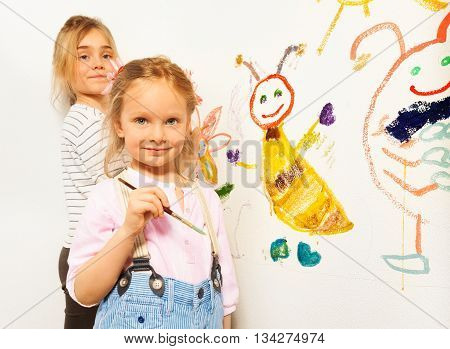 Two little girls with brushes drawing funny bugs, isolated on white