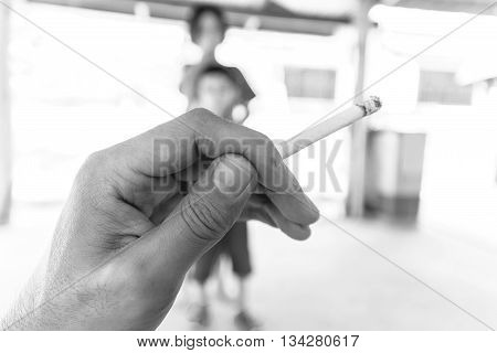 Focus at cigarette in hand with burred of choldrens background;Concept for World No Tobacco Day.