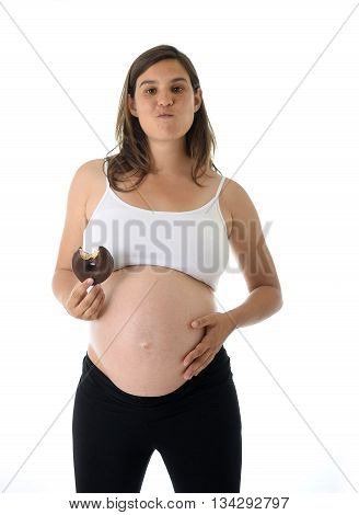 young attractive pregnant woman holding her big belly in one hand and eating chocolate donut happy isolated on white background in pregnancy whim food concept isolated on white background