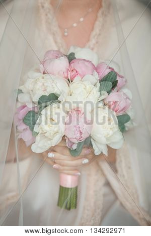 Charming and delicate bride holding bouquet with peonies and eucalyptus. Pink and white peonies under the veil of the bride