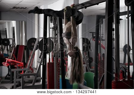 Young sexy fitness girl pulls up in the gym and performing exercises on the horizontal bar. Toning image