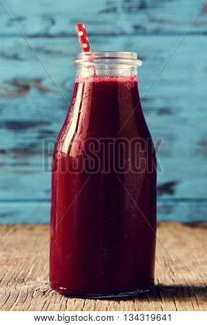 closeup of a red detox smoothie served in a glass bottle with a red drinking straw patterned with white dots, on a rustic wooden surface