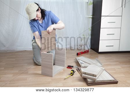 Installation of wooden furniture made of particle board in the home the woman assemble drawer.