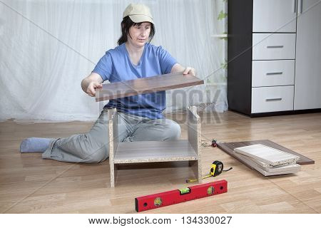 Self  assembly of furniture a housewife assembles nightstand in the interior of the apartment sitting on the floor.