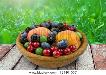 fruits and berries in a wooden plate gooseberry blackbery peach blueberry. on nature background