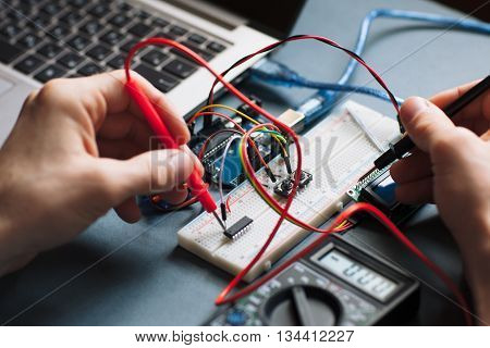 Single board microcontroller testing close-up. Electrical tester units in engineer hands, working with microcontroller, connected to laptop on black background
