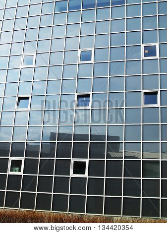 Glass wall of a building with big squre mirror windows at natural lightning. Reflections of sky and surrounding in glass windows