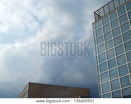 Tall building with big squre mirror windows at natural lightning. Reflections of sky and rain clouds in glass windows