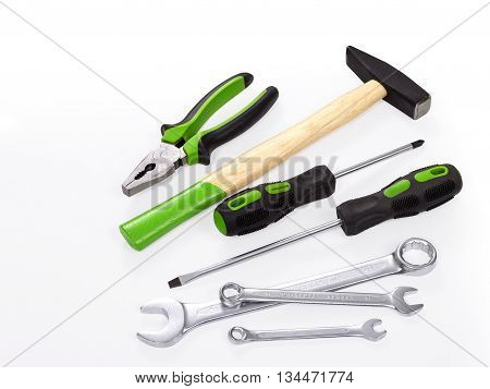 The hammer, spanner, pliers and screwdrivers on a white background. Hammer with wood handle. The back end handle paited in green color. Screwdriver and pliers with grenn piece