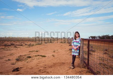Young girl leaning on a fence in the dry drought ridden outback australia