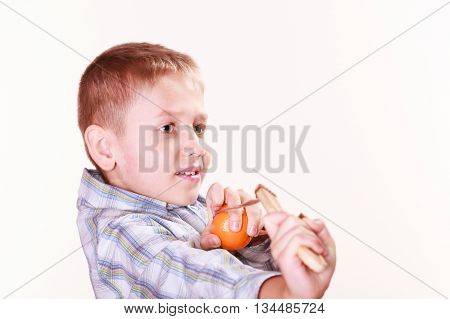 Nature and free time prankster little boy. Child have fun with wooden sling shot and fruit aim mandarine.