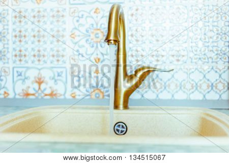 Golden faucet to the sink in the kitchen with tiled floors.