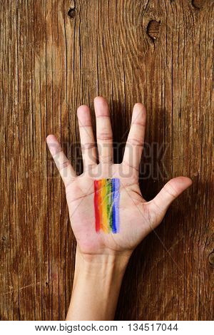 closeup of a young caucasian man with a rainbow flag painted in the palm of his hand against a rustic wooden background