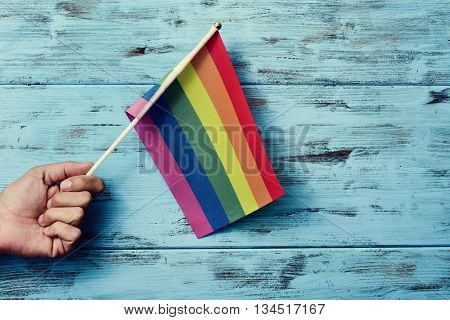 closeup of a young caucasian man waving a small rainbow flag against a rustic blue wooden background