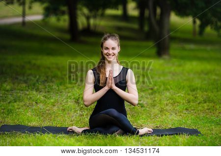 Portrait of smiling beautiful sporty young woman working out in park alley, standing with palms touching in Namaste gesture.
