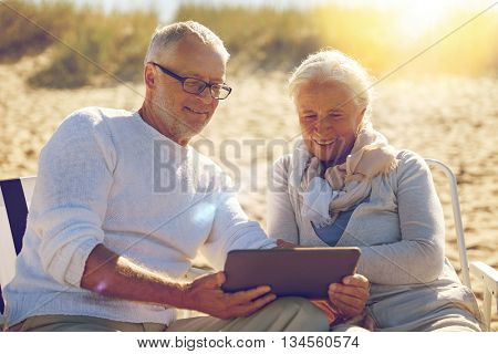 family, age, travel, tourism and people concept - happy senior couple with tablet pc computer resting in folding chairs on summer beach