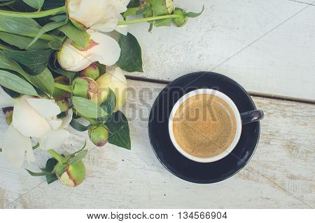 Coffee and flowers peony. A cup of coffee and Peonies on a white wooden table. Breakfast on Mothers day, Valentines Day or Womens day. Spring or summer background. Copy space. Top view. Toned image.