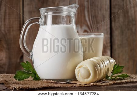 Natural rustic whole milk in a glass jug and a glass suluguni cheese and parsley leaves on the old wooden background closeup