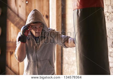 Young Male Boxer Working Out With Punchbag In Gym