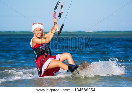 Beautiful young girl on the kite in the costume of Santa Claus. Christmas and New year on a tropical island. Extreme Sport Kitesurfing