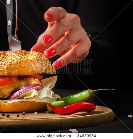 Homemade delicious juicy burger. The girl is going to eat the burger. Burger with women's hands on a dark background.
