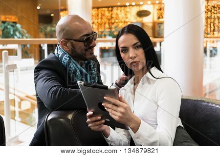 Arab man and stylish girl looking photos on digital tablet in shopping centre