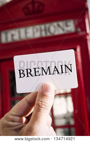 the hand of a young man showing a signboard with the text Bremain with a red telephone booth in the background, in London, UK