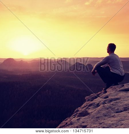 Adult In Black Trousers, Jacket Sit On Cliff's Edge