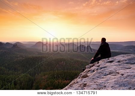 Adult In Black Trousers, Jacket Sit On Cliff's Edge