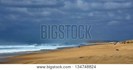 Horizontal landscape of the beach with a fisherman, shipwreck in the background and dramatic clouds (Stockton Beach, NSW, Australia)